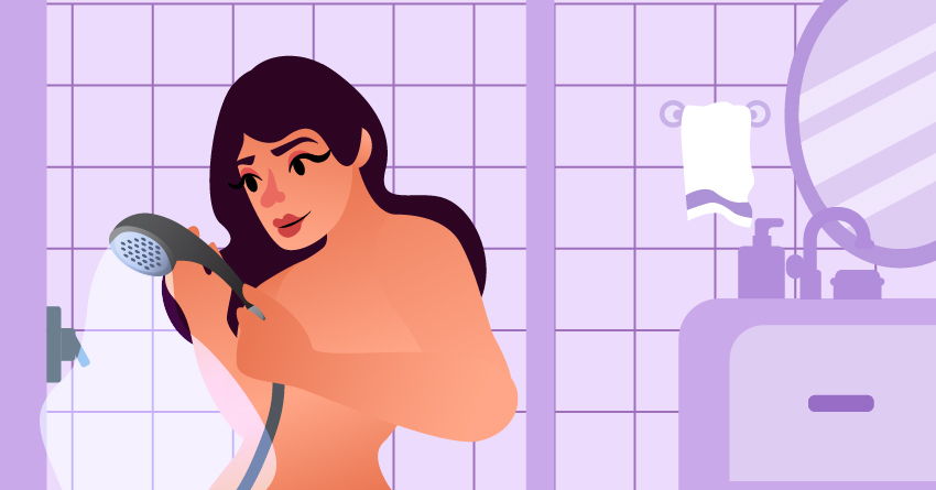 A naked woman holding a detachable showerhead. 